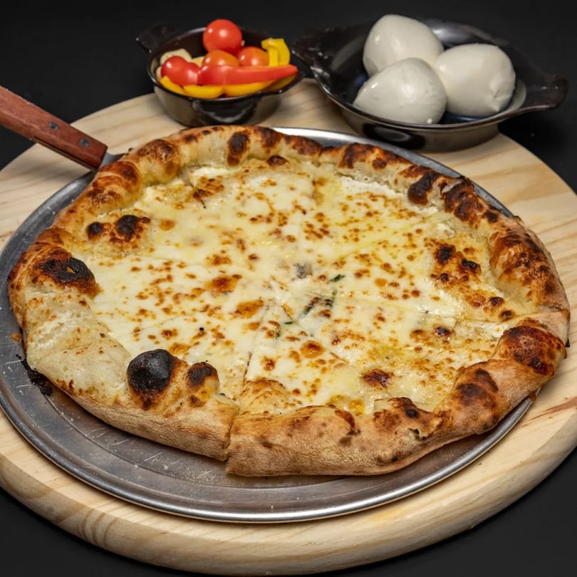 A cheese pizza on a metal pan and wooden board, with cherry tomatoes and mozzarella balls.