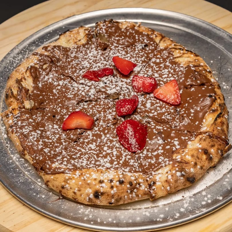 Nutella pizza with powdered sugar and strawberry slices on a metal tray.