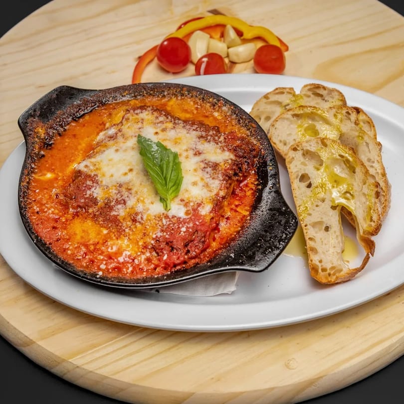 Baked pasta with melted cheese and tomato sauce, garnished with basil, served with bread.